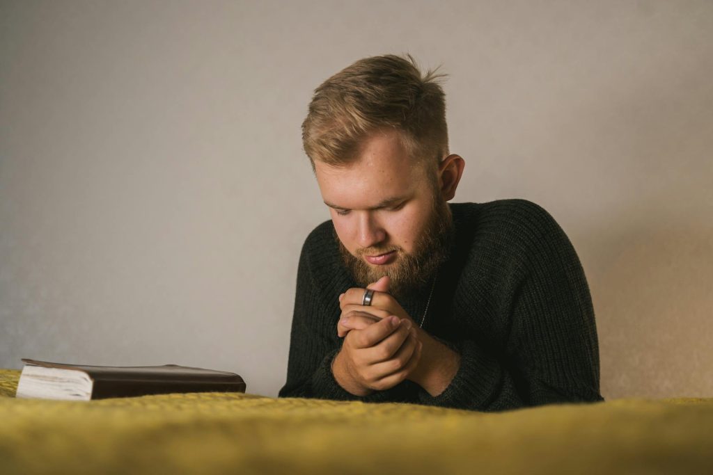 A man kneeling beside his bed to pray.