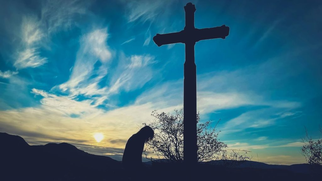 A man kneeling in front of a cross.