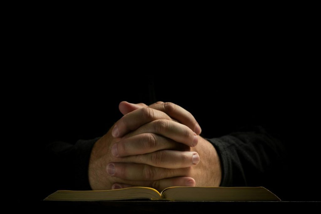 Hands clasped for praying on top of an open book